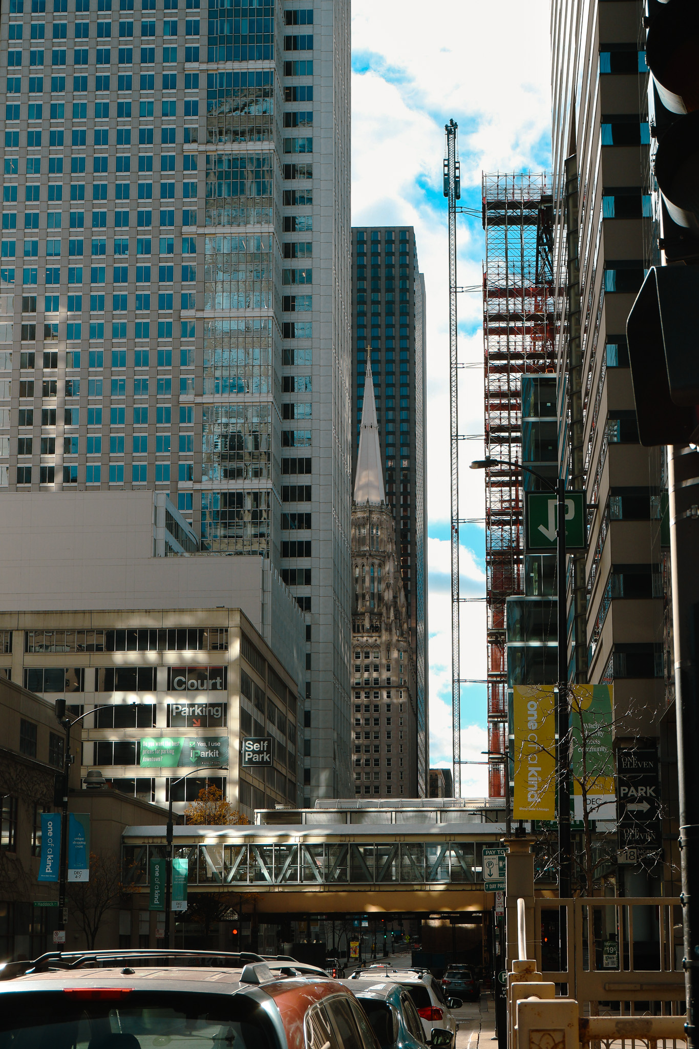 Downtown city corridor with traffic, glass towers, and a distant church spire.