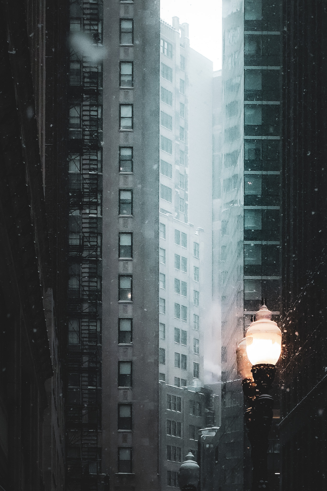 Snowy urban alley framed by tall buildings and a glowing street lamp.